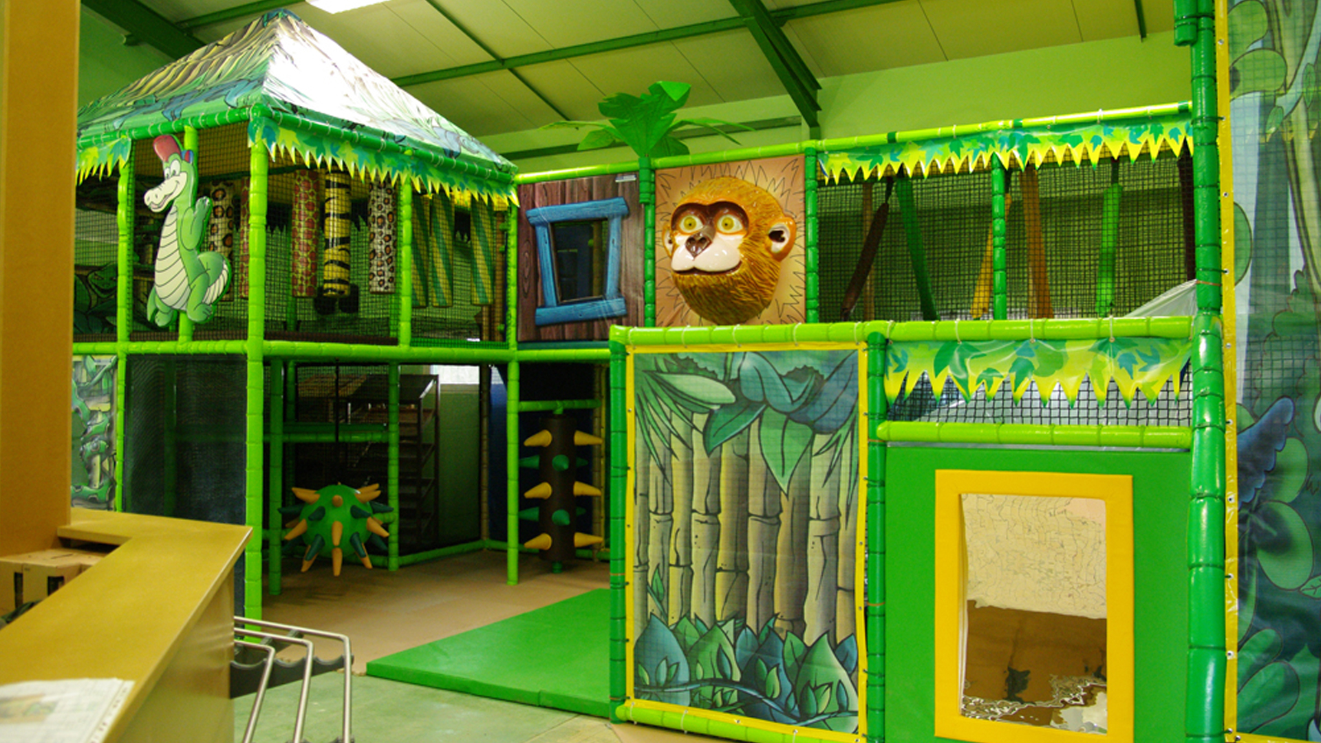 Indoor jungle-themed playground with climbing areas and a monkey face decoration on the wall.