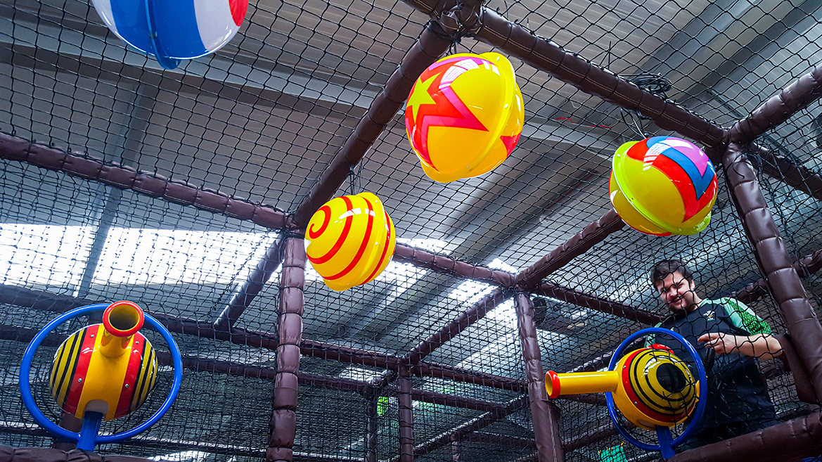 Inside a indoor play area, a man is surrounded by numerous colourful balls