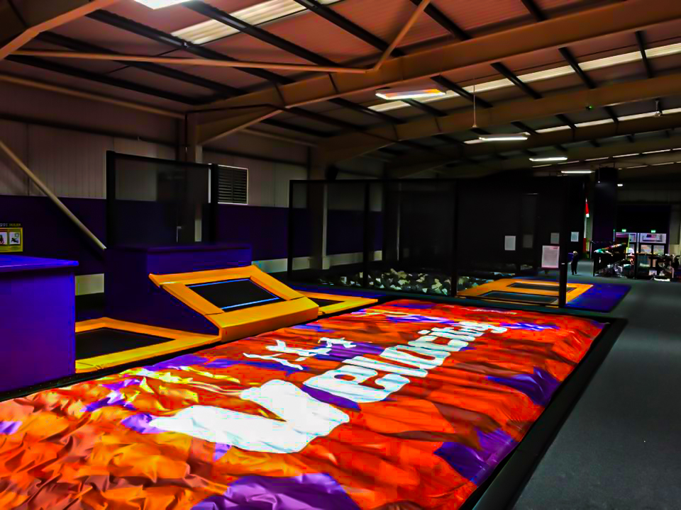 A large air bag surrounded by trampolines in an indoor trampoline park.